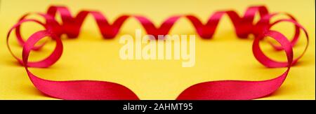 Frame of red ribbon on yellow background. Festive substrate for holiday invitation. Stock Photo