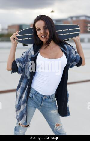 Happy young trendy urban woman posing with longboard behind her head Stock Photo
