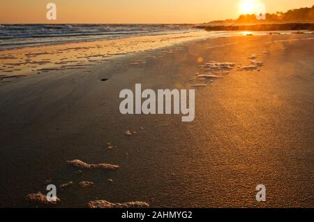 Sun rising over Atlantic Ocean and Yeu island horizon, the sun is coloring the wet sand of the beach in golden colors, pieces of foam are following th Stock Photo