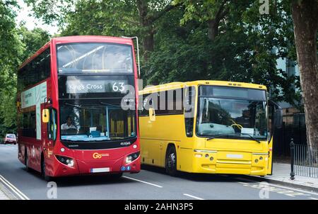 A red London bus alongside a bright yellow coach waiting to collect passengers for a trip. Stock Photo