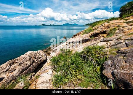 Wild stone western coast of Ko Samet Island in the gulf of Thailand in Thai province Rayong. The mainland and the cloudy sky is at background Stock Photo