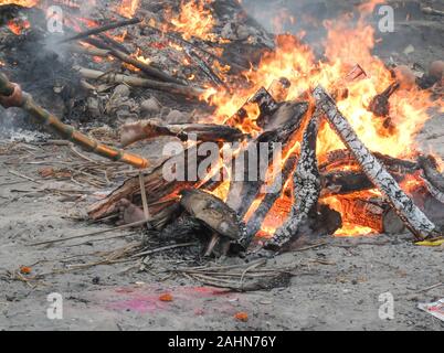 The intense heat,smoke and odors are overwhelming as a worker nearby tends a pyre with a bamboo pole and body parts are visible while Hindu corpses ar Stock Photo