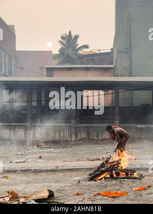 PURI,ODISHA/INDIA-MARCH 12 2018:Toward sunset,a worker tends the pyre of a Hindu person at Swargadwar crematorium next to the main beach.A steady flow Stock Photo