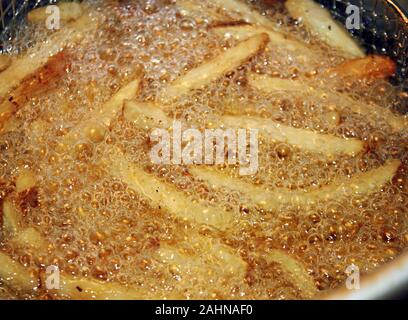 French fries cooking and bubbling in a deep fryer filled with oil Stock Photo