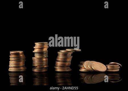 Coin stacks reflected isolated on a black background with plenty of copy space. Reflected penny towers collapsing, economy concept. Stock Photo