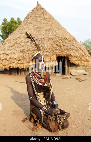 Omo valley, Karo tribe man with painted face, decoration of shells, fur and animal skin sitting in front of a traditional house, Ethiopia, Africa Stock Photo