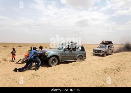 Armed men push their car stuck in soft sand near Lake turkana, border of Ethiopia and Kenya Stock Photo