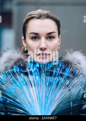 Portrait of young woman with a bunch of glowing optical fibers in her hands looking at camera. Concept of global new telecommunication technology. Fas Stock Photo