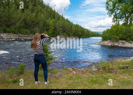 Young woman is photographing the landscape in the border of Fugga river in Hedmark county of Norway. Close to Akrestrommen village in Rendalen municip Stock Photo