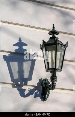 A lantern in the sun casts a shadow on a white wooden wall Stock Photo