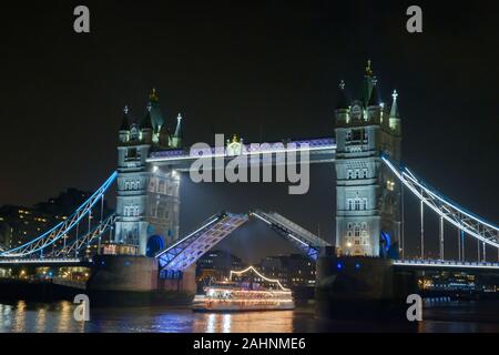 Iconic Tower Bridge lit up at night, lifting to allow brightly lit vessel pass through, on River Thames, London. Stock Photo