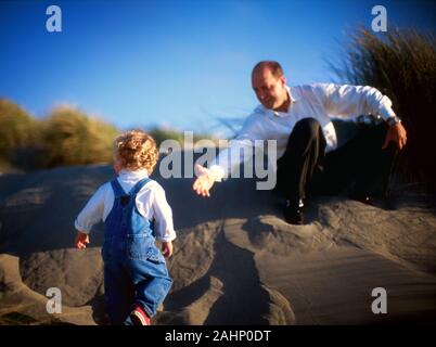 A father is helping his son climb a slope at the shore. Stock Photo