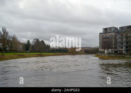 The swollen River Kent nearly bursting its banks showing an apartment block on the river bank with trees beyond all under a cloudy, grey sky Stock Photo