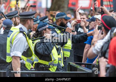 Police officers, including a male officer with Muslim features defending Downing Street, Whitehall, London, UK, with batons raised during Brexit rally Stock Photo