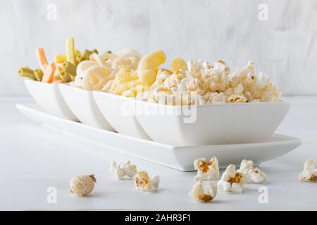 A horizontal view of a row of white dishes filled with healthy puff snacks with the popcorn overflowing. Stock Photo