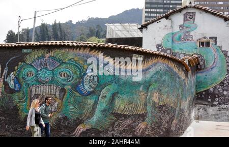 Couple walking past street art ('Monstrucation') and graffiti painted on wall and exterior of building in La Candelaria district of Bogota, Colombia Stock Photo