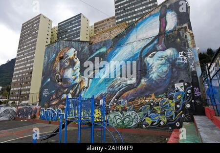Mural by urban artist Bastardilla and graffiti on exterior of residential building behind playground in La Candelaria district of Bogota, Colombia Stock Photo