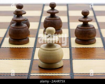Underdog Concept: One White Pawn Standing Against Four Black Pawns On A Chess Board Stock Photo