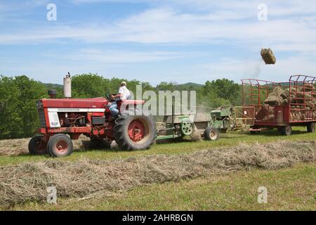 Man on International Harvester Farmall tractor, baling hay in a field with a bale flying in the air, in Galena, Illinois, USA.  (For editorial use onl Stock Photo