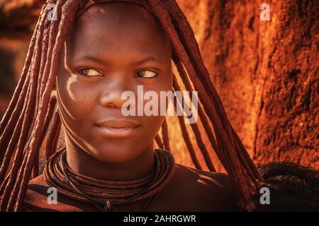 Rural Namibia - Aug 22, 2016. A young African woman wears the traditional hairstyle, leather necklaces, and ochre-tinted skin paste of the Himba tribe Stock Photo