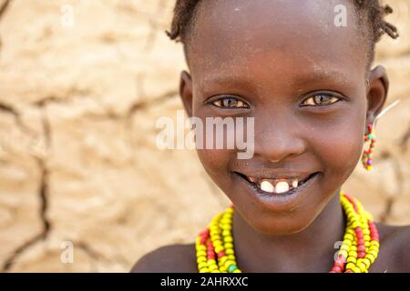 Portrait of a girl from Dassanech tribe in front of a cracked walls of a traditional house, Omo valley, Ethiopia Stock Photo