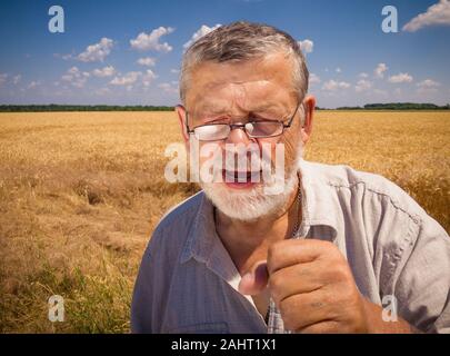 Outdoor portrait of Caucasian senior farmer singing like in karaoke while standing against wheat field at summer season Stock Photo