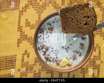 Top view on a bowl with cooked buckwheat with milk standing on a checkered tablecloth Stock Photo