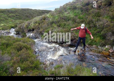 Lone Man Crossing Fast Flowing Burn to the Scottish Mountain Corbett Meall Dubh, Glen Moriston, Scottish Highlands, Scotland, UK. Stock Photo