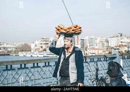 Turkey, Istanbul, December 29, 2019 - The seller walks along the Galata bridge and bears on his head many traditional Turkish bagels Simit. Street food business. Stock Photo