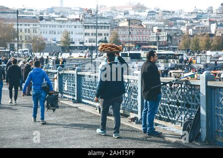 Turkey, Istanbul, December 29, 2019 - The seller walks along the Galata bridge and bears on his head many traditional Turkish bagels Simit. Street food business. Stock Photo