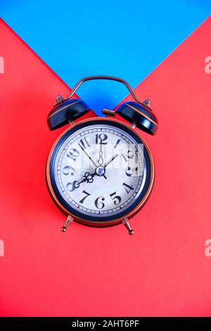Old retro alarm clock on red and blue background. Stock Photo