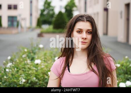 street portrait of a serious young woman with long brunette hair outdoor. Beautiful young female in an urban setting with copy space Stock Photo