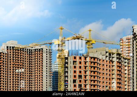 two yellow construction cranes at the construction site of multi-storey brick houses against blue sky. Stock Photo
