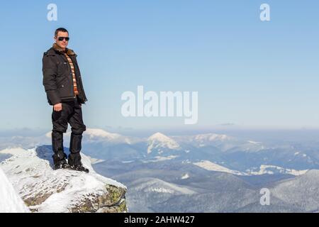Silhouette of alone tourist standing on snowy mountain top enjoying view and achievement on bright sunny winter day. Adventure, outdoors activities an Stock Photo