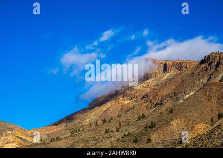 Spain, Tenerife, Rocky caldera desert near mountain teide volcano in winter with blue sky and foggy mood Stock Photo