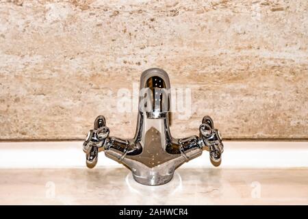 Chrome metallic faucet and sink in bathroom against background of marble wall. Front view. Stock Photo