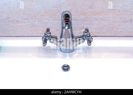 Chrome metallic faucet and sink in bathroom against background of marble wall. Front view. Stock Photo