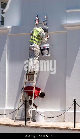 St James, Cape Town, South Africa.  Two painter decorators paint a wall white in bright sunlight. Stock Photo