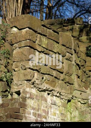 old quarry stone wall with a foundation of bricks. Blue sky and trees in the blurred background Stock Photo