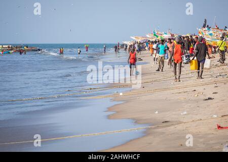 TANJI, THE GAMBIA - NOVEMBER 21, 2019: Scene with men and women carrying fish from the boats to the beach on Tanji, Gambia, West Africa. Stock Photo