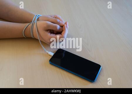 Woman's hands tied to the smartphone by the battery charging wire. Smartphone and technology addiction concept Stock Photo