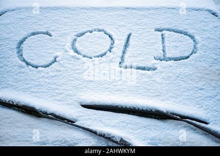 The word cold written on a frozen car screen. Cold written on front windshield of a car. Word cold over car wipers. Cold inscription written on a frosted car windscreen. Snowy background. Meteorology Stock Photo