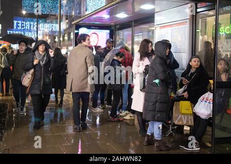 London, UK - 20 December 2019, People waiting for a bus on a crowded street on Oxford Street at night in the rain. Stock Photo