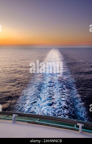A shot of the ships wake taken from the rear or stern of a ship as it sales across the sea at sunset. Stock Photo