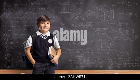 Schoolboy with books and backpack standing in front of a blackboard with math formulas Stock Photo