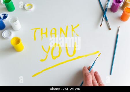 Top view of woman hand painting 'Thank you' text on white background, artistic creative occupation Stock Photo