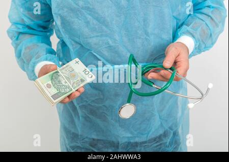 Doctor hands holding pile of Polish money banknotes and  stethoscope. Medical services financial concept Stock Photo