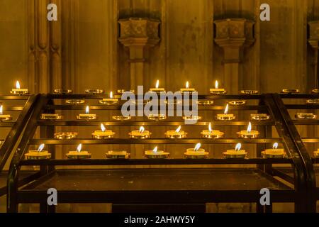 A votive candle rack or prayer candle rack with rows of flickering lit candles. Stock Photo