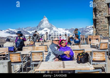 A Chinese couple sitting at a restaurant terrace takes a selfie with the Matterhorn mountain. Gornetgrat, Switzerland Stock Photo