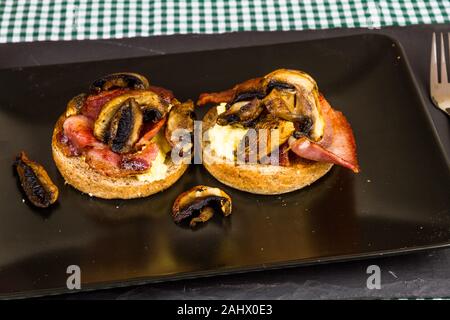 Breakfast dish of bacon, scrambled eggs and mushrooms on brown bread muffins. Stock Photo
